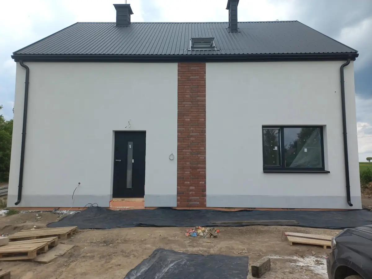 Nowy dom z białą elewacją, pasem cegły przy wejściu i grafitowym dachem