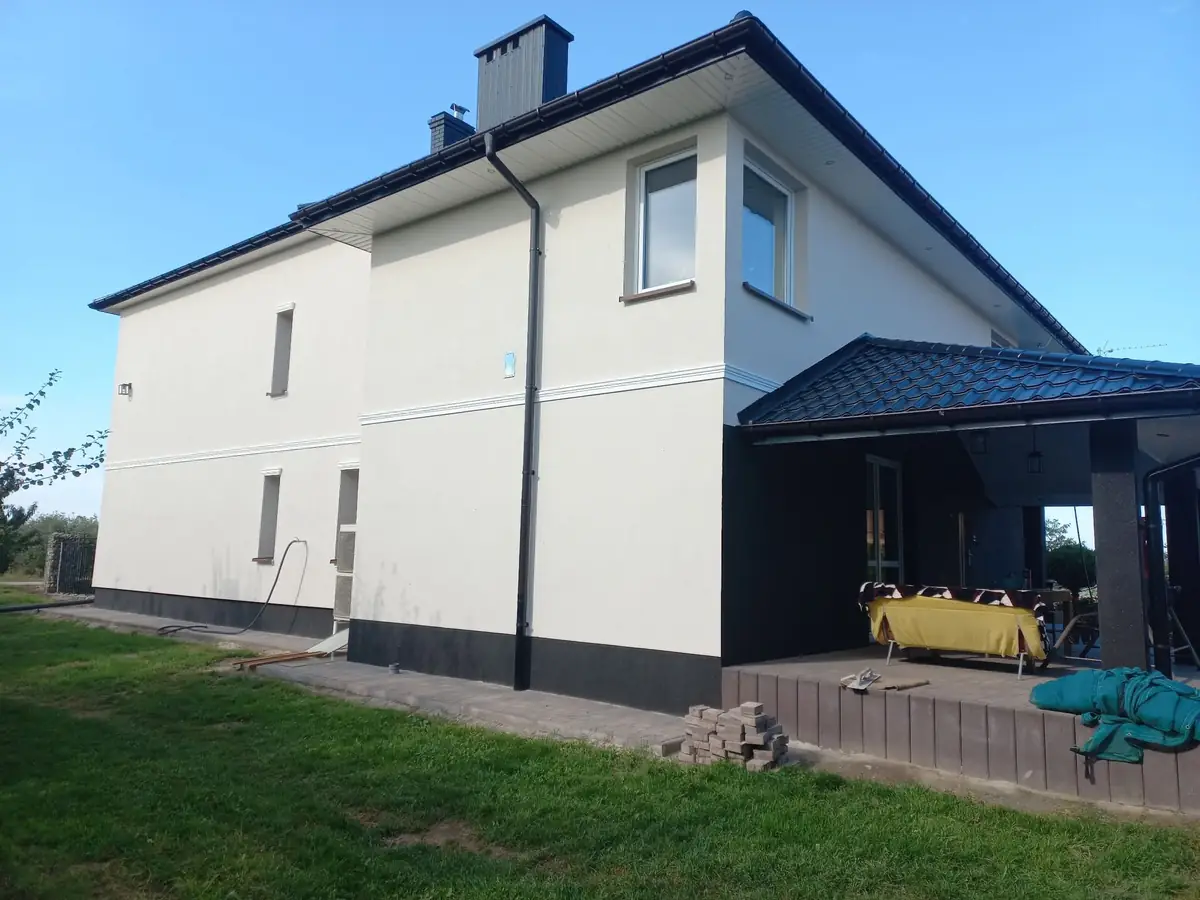 Piętrowy dom z jasną elewacją, ciemnym cokołem i zadaszonym tarasem