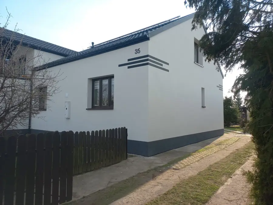 Biała elewacja z szarymi poziomymi pasami przy szczycie i grafitowym cokołem